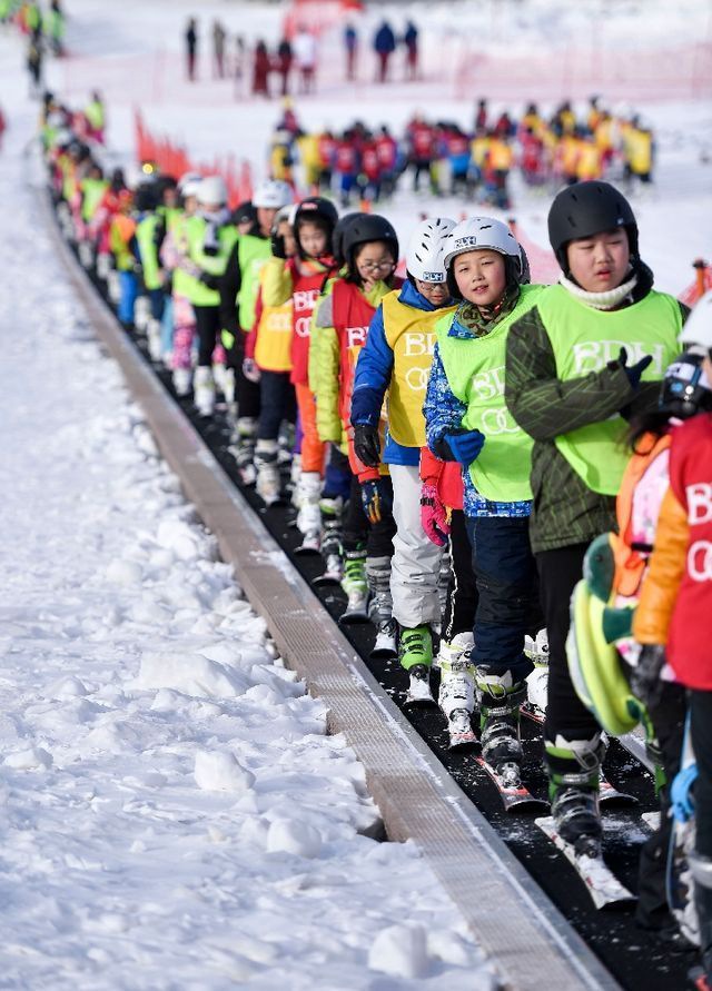 在吉林北大壺滑雪場,吉林市第二實驗小學學生們在滑雪教練的帶領下乘坐“魔毯”前往雪場學習區域。